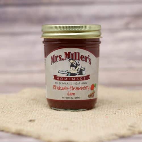 A 9 oz glass jar of Mrs. Miller's No Sugar Added Rhubarb Strawberry Jam, on rustic burlap with a wooden background.