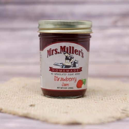 A 9 oz glass jar of Mrs. Miller's no sugar added Strawberry Jam, on rustic burlap with a wooden background.