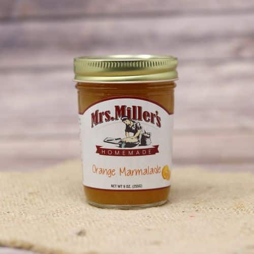 A 9 oz glass jar of Mrs. Miller's Orange Marmalade, on rustic burlap with a wooden background.