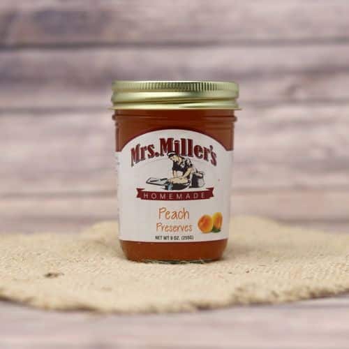 A 9 oz glass jar of Mrs. Miller's Peach Preserves, on rustic burlap with a wooden background.