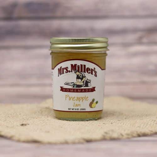 A 9 oz glass jar of Mrs. Miller's Pineapple Jam, on rustic burlap with a wooden background.
