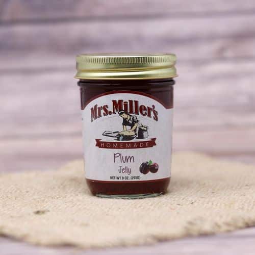 A 9 oz glass jar of Mrs. Miller's Plum Jelly, on rustic burlap with a wooden background.