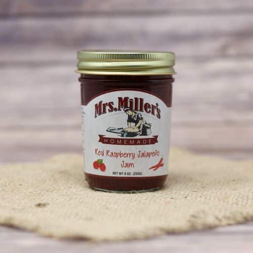 A 9 oz glass jar of Mrs. Miller's Red Raspberry Jalapeno Jam, on rustic burlap with a wooden background.