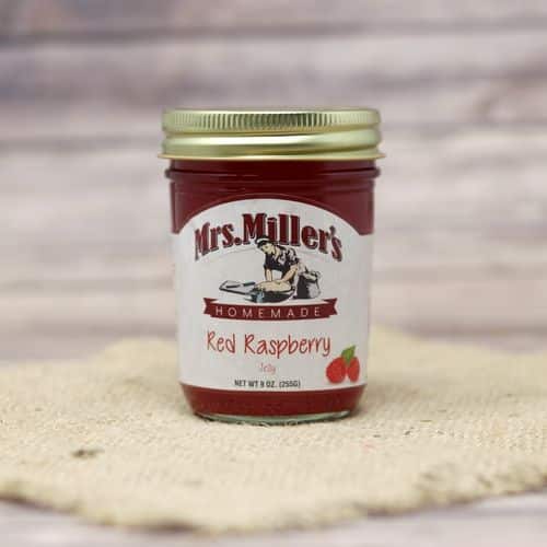 A 9 oz glass jar of Mrs. Miller's Red Raspberry Jelly, on rustic burlap with a wooden background.