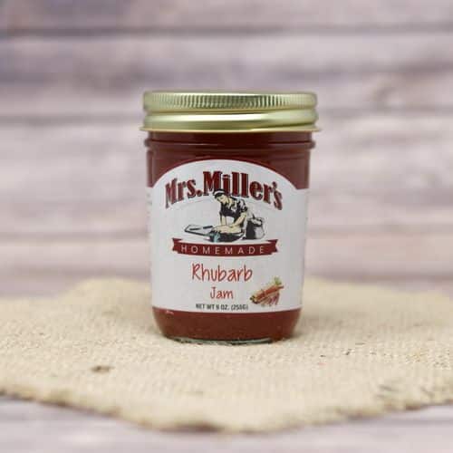 A 9 oz glass jar of Mrs. Miller's Rhubarb Jam, on rustic burlap with a wooden background.