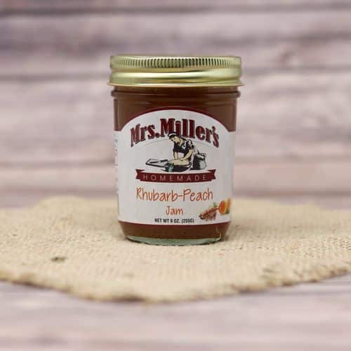 A 9 oz glass jar of Mrs. Miller's Rhubarb Peach Jam, on rustic burlap with a wooden background.