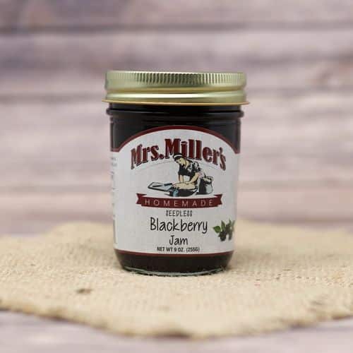 A 9 oz glass jar of Mrs. Miller's Seedless Blackberry Jam, on rustic burlap with a wooden background.
