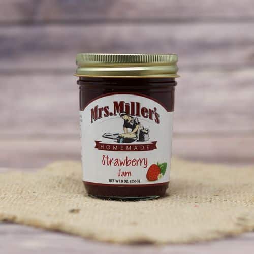 A 9 oz glass jar of Mrs. Miller's Strawberry Jam, on rustic burlap with a wooden background.