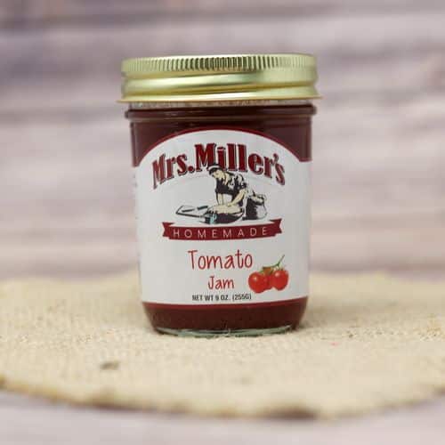 A 9 oz glass jar of Mrs. Miller's Tomato Jam, on rustic burlap with a wooden background.