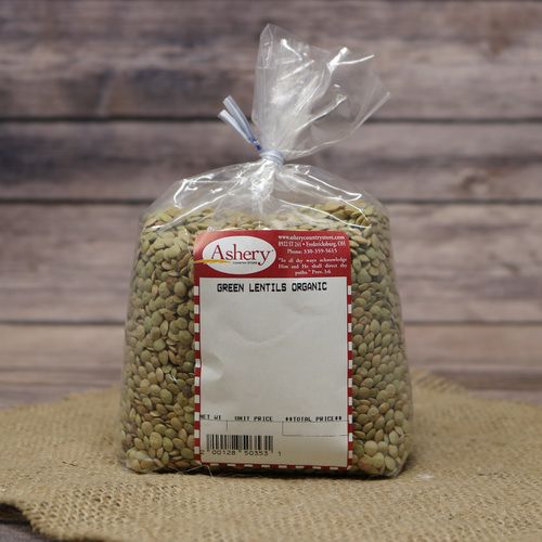 A bag of Green Lentils Organic in a clear plastic bag sealed with a twist tie on rustic burlap with a wooden background.