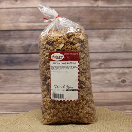 A clear plastic bag sealed with a red twist tie of Honey Almond Granola on rustic burlap with a wooden background.