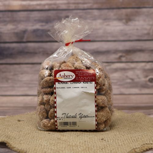 A clear plastic bag of Cinnamon Roasted Almonds, closed with a twist tie and set on rustic burlap with a wooden background.