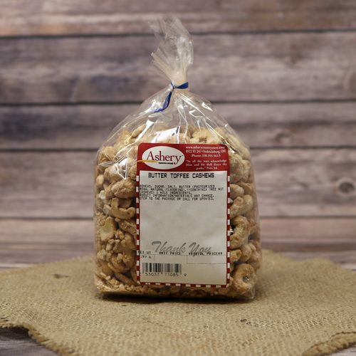 A clear plastic bag of Butter Toffee Cashews, closed with a twist tie and set on rustic burlap with a wooden background.