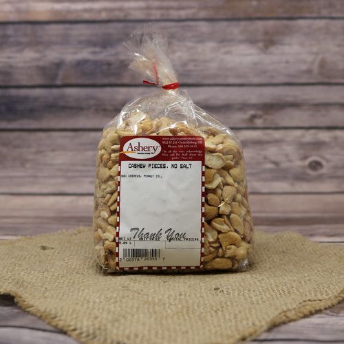 A clear plastic bag of Cashew Pieces No Salt, closed with a twist tie and set on rustic burlap with a wooden background.