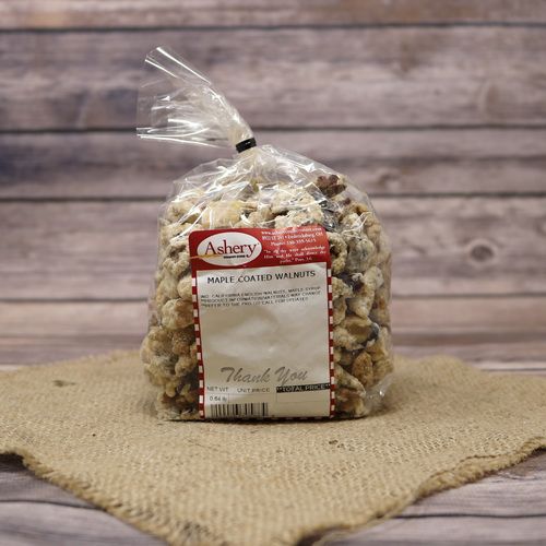 A clear plastic bag of Maple Coated Walnuts, closed with a twist tie and set on rustic burlap with a wooden background.