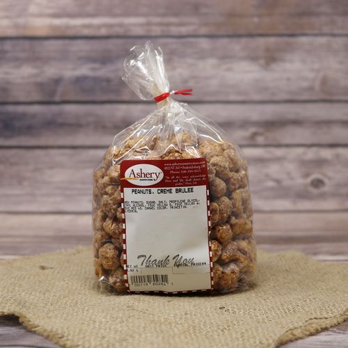 A clear plastic bag of Creme Brulee Peanuts, closed with a twist tie and set on rustic burlap with a wooden background.