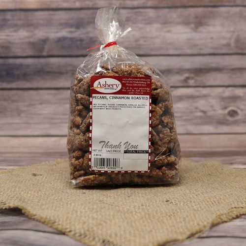 A clear plastic bag of Cinnamon Roasted Pecans, closed with a twist tie and set on rustic burlap with a wooden background.