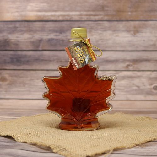 A leaf shaped glass bottle of Pure Ohio Maple Syrup, set on rustic burlap with a wooden background.