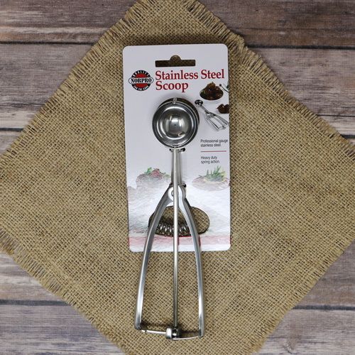 A stainless steel Cookie Scoop, laying on rustic burlap with a wooden background.