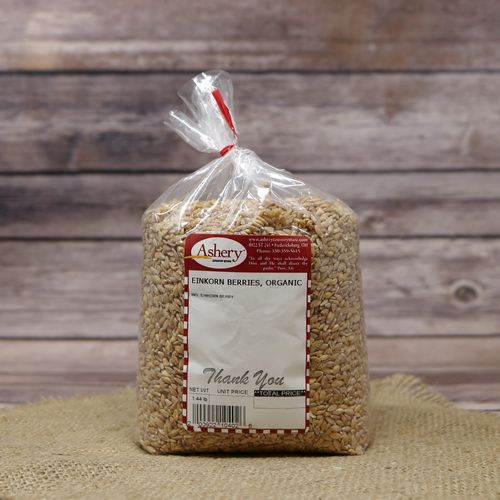 A bag of Einkorn Wheat Berries Organic, sealed with a twist tie, on rustic burlap with a wooden background.