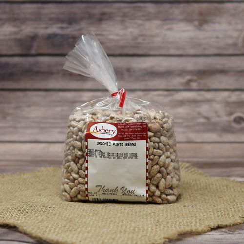 A clear plastic bag of Organic Pinto Beans on rustic burlap with a wooden background.