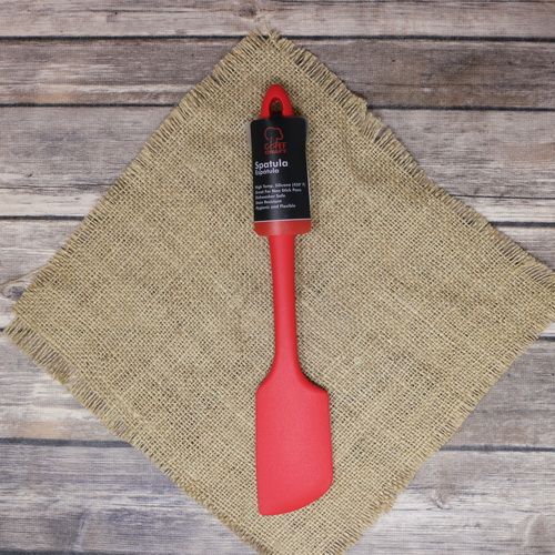 A red Silicone Spatula, laying on rustic burlap with a wooden background.