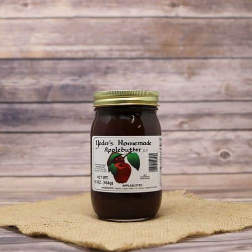 A 16oz glass jar of Yoder's Homemade Apple Butter, on rustic burlap with a wooden background.