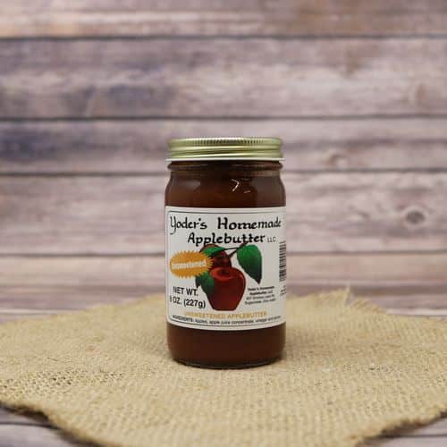 An 8oz glass jar of Yoder's Homemade Unsweetened Apple Butter, on rustic burlap with a wooden background.