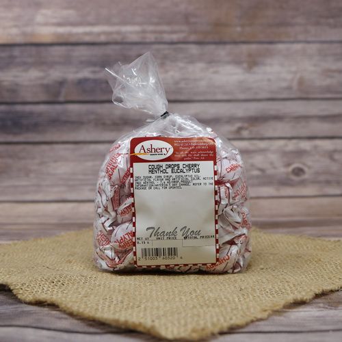 A clear plastic bag filled with Cherry Menthol Cough Drops and closed with a twist tie, set on rustic burlap with a wooden background.