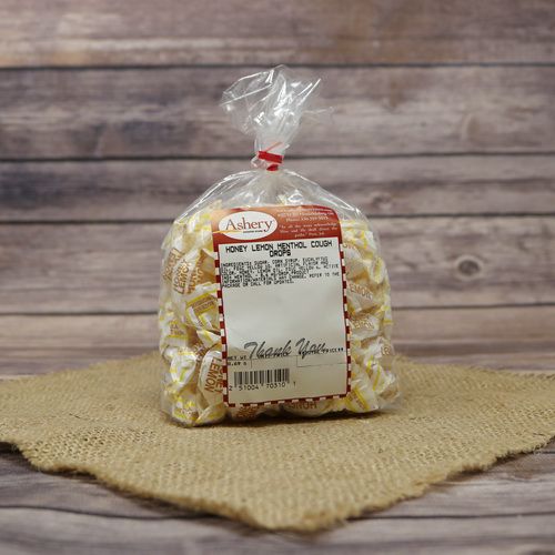A clear plastic bag filled with Honey Lemon Cough Drops and closed with a twist tie, set on rustic burlap with a wooden background.
