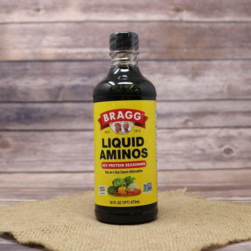 A 16oz bottle of Bragg's Liquid Aminos, set on rustic burlap with a wooden background.