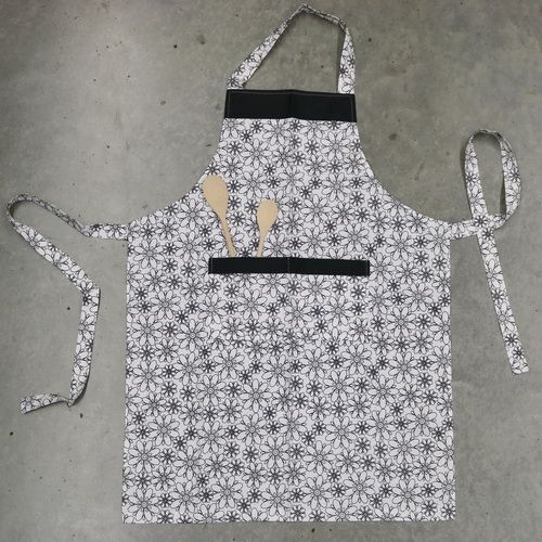 An apron that has a front pocket and is made with black and white flowers fabric.