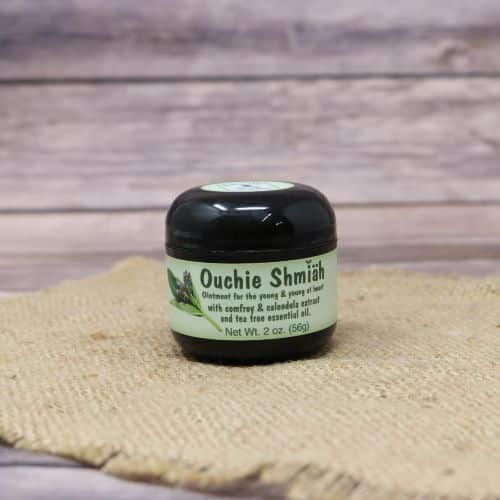 A 2 oz container of Ouchie Ointment, set on rustic burlap with a wooden background.