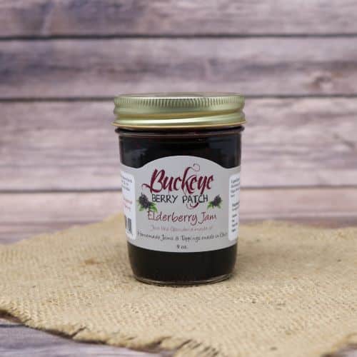 A 9oz glass jar of Buckeye Berry Patch Elderberry Jam, on rustic burlap with a wooden background.