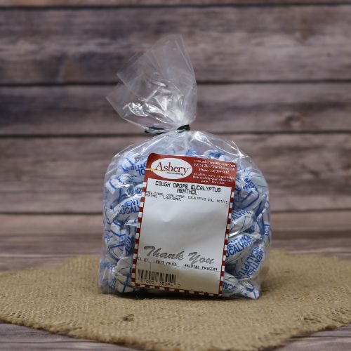 A clear plastic bag with the Ashery label with Eucalyptus Cough Drops inside, set on rustic burlap with a wooden background.