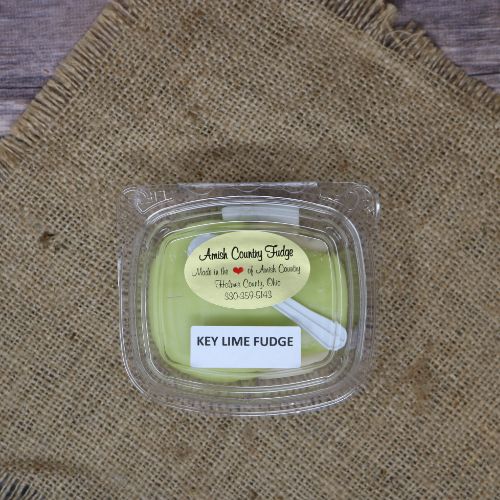 Clear plastic Ashery bowl with yellow sticker label on the plastic lid, filled with green key lime fudge, sitting on a burlap material with wood background