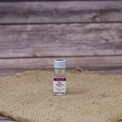 small clear bottle with a red and white label and a sealed lid, with a clear liquid in it, sitting on a burlap material with wood background