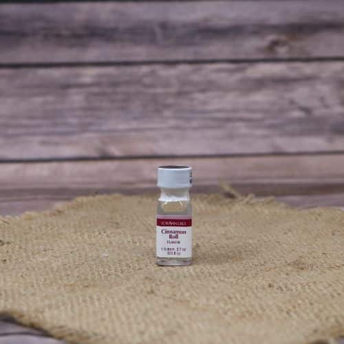 small clear bottle with a red and white label and a sealed lid, with a clear liquid in it, sitting on a burlap material with wood background