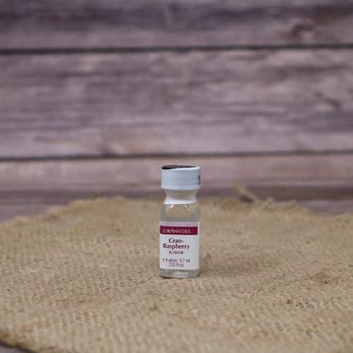 small clear bottle with a red and white label and a sealed lid, with a clear liquid in it, sitting on a burlap material with wood background