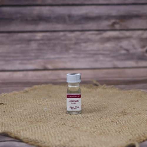 small clear bottle with a red and white label and a sealed lid, with a clear liquid in it, sitting on a burlap material with wood background