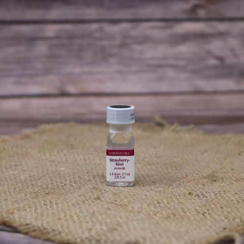 small clear bottle with a red and white label and a sealed lid, with a clear liquid in it, sitting on a burlap material with wood background