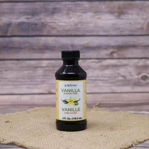 Small 4oz black bottle of liquid with a white and yellow sticker label, sitting on a burlap material with wood background
