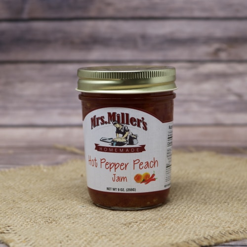 A 9oz glass jar of Mrs. Miller's Hot Pepper Peach Jam, on rustic burlap with a wooden background.