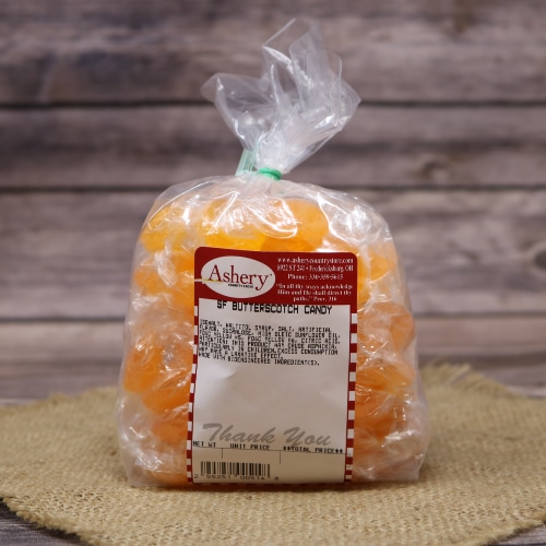 A clear bag of Ashery sugar-free butterscotch candy, showcasing the individually wrapped orange and yellow sweets, on a straw mat background.