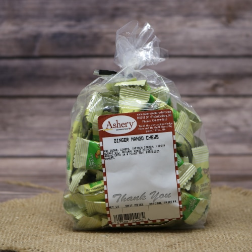 A clear plastic bag of Ginger Mango Chews with the Ashery label on them, set on rustic burlap with a wooden background.