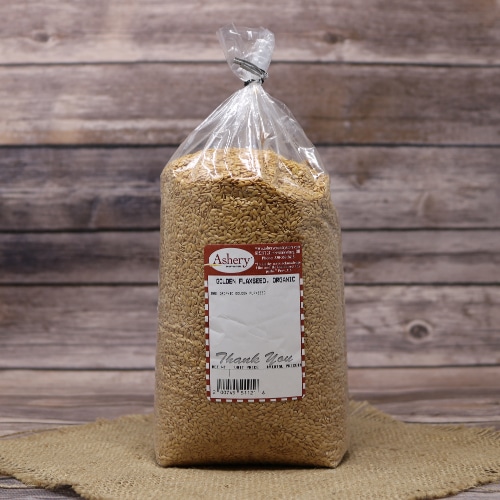 A plastic bag of Organic Golden Flax seeds closed with a twist tie, set on rustic burlap with a wooden background.
