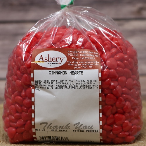Bag of Ashery's Cinnamon Hearts Candy in vibrant red, sealed with a twist tie, on a rustic burlap and wooden background.