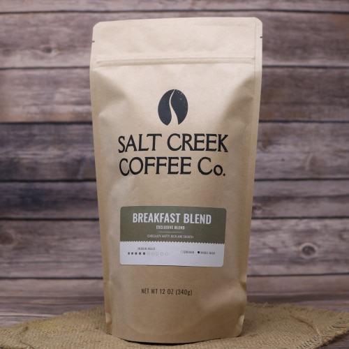 A brown bag of Breakfast Blend Whole Bean Coffee on rustic burlap with a wooden background.