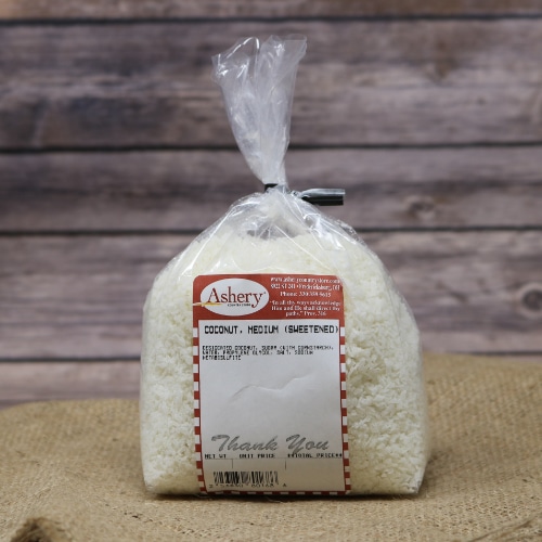A clear plastic bag of Coconut Medium Sweetened sealed with a black twist tie on rustic burlap with a wooden background.