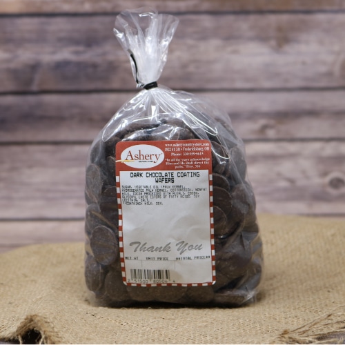 A clear plastic bag of Merckens Dark Chocolate Coating Wafers sealed with a black twist tie on rustic burlap with a wooden background.